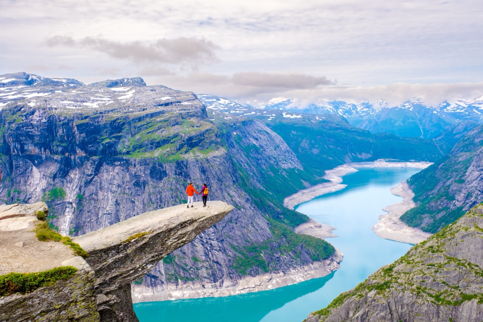 Two hikers standing on the end of Trolltunga above the lake