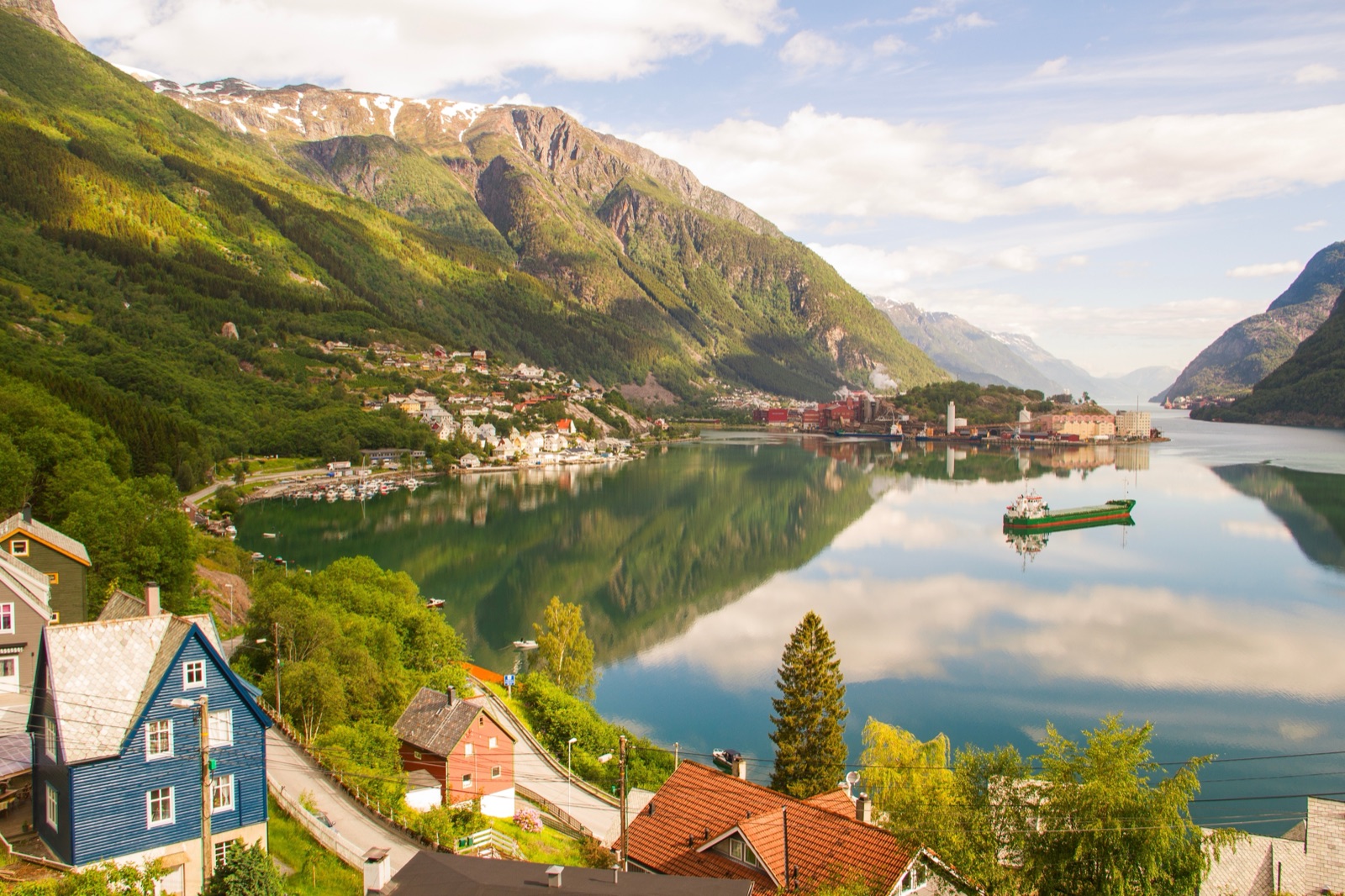 Houses and a quay on the fjord at Odda, reflected in still water below green mountains